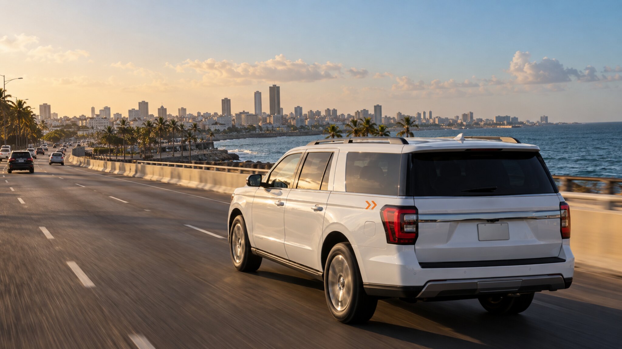 A white chauffeur SUV on the Santo Domingo Malecón at sunset, the city skyline and the Caribbean beyond