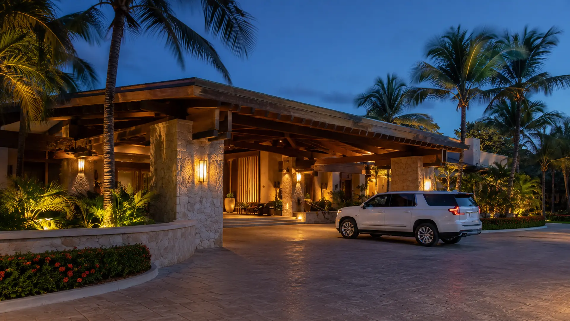 A white SUV waiting under the lit stone-and-timber arrival portico of a Punta Cana resort at dusk