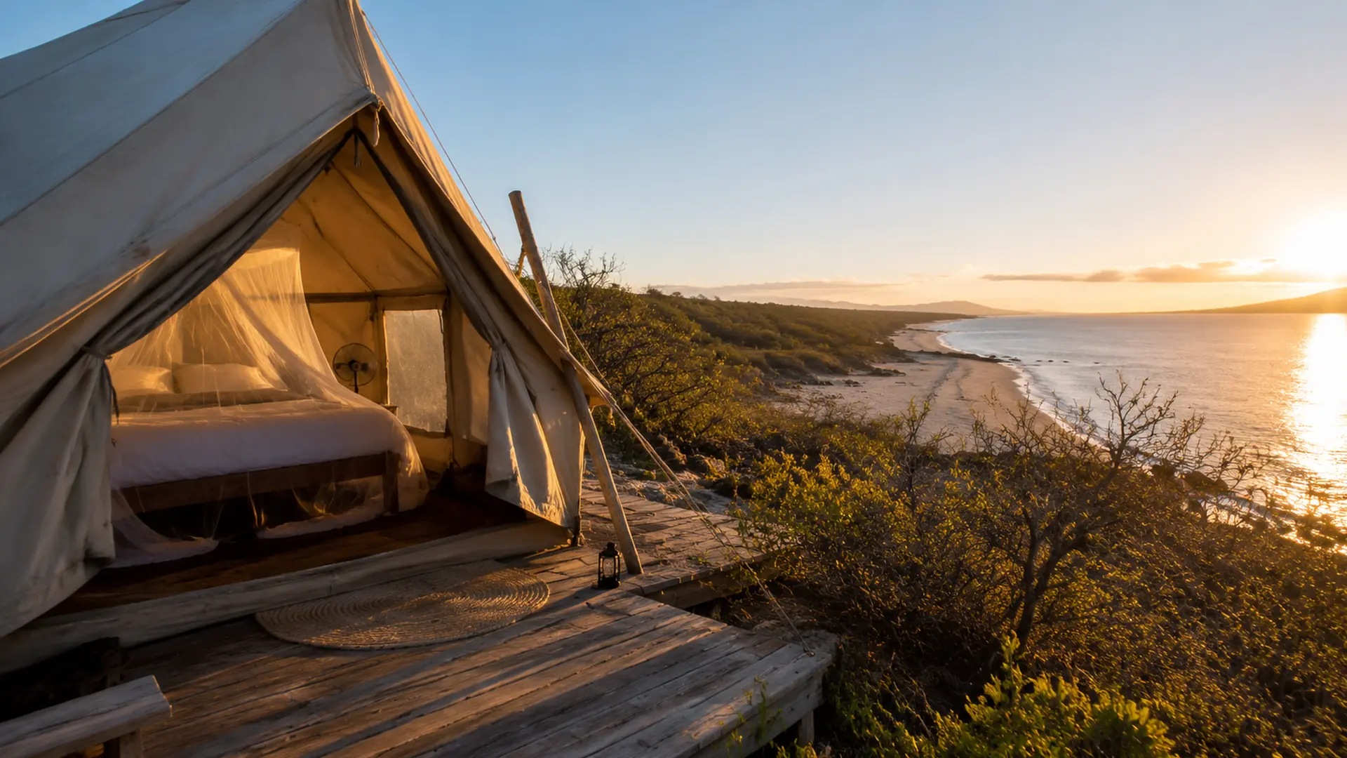 A canvas glamping tent on a wooden deck overlooking the dry coastal scrub and shoreline of Pedernales at sunrise
