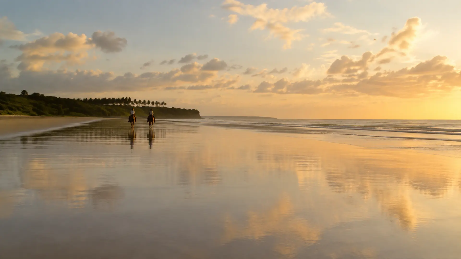 Two horseback riders on a wide reflective beach near Las Galeras at sunset