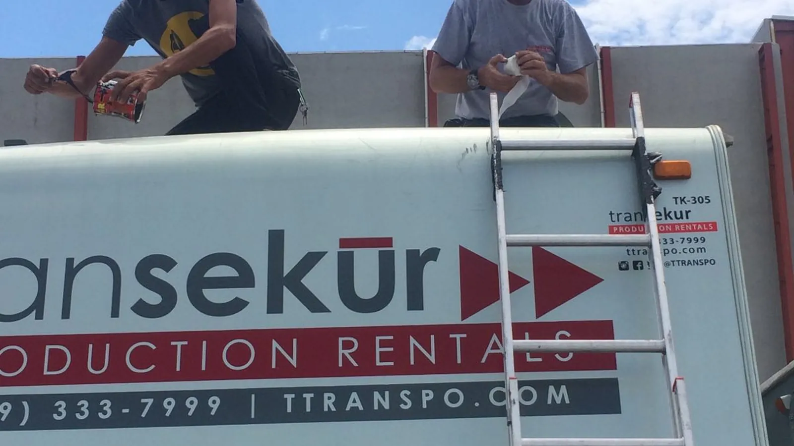 Deux employés de Transekur sur une échelle en train de poser le marquage Transekur Production Rentals sur le flanc d'un fourgon