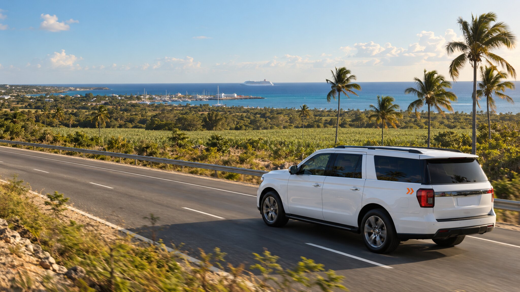 A white chauffeur SUV on a coast road above cane fields, with a marina, moored yachts and a cruise ship offshore in the distance