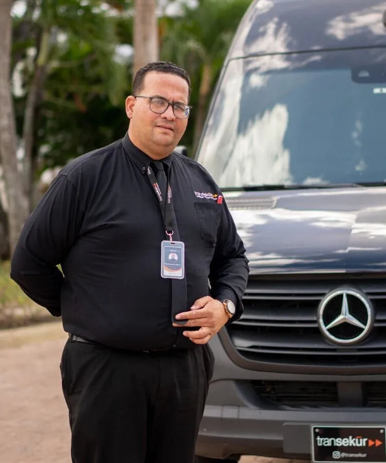 A Transekur chauffeur in a black uniform with company ID badge standing in front of a Mercedes Sprinter van
